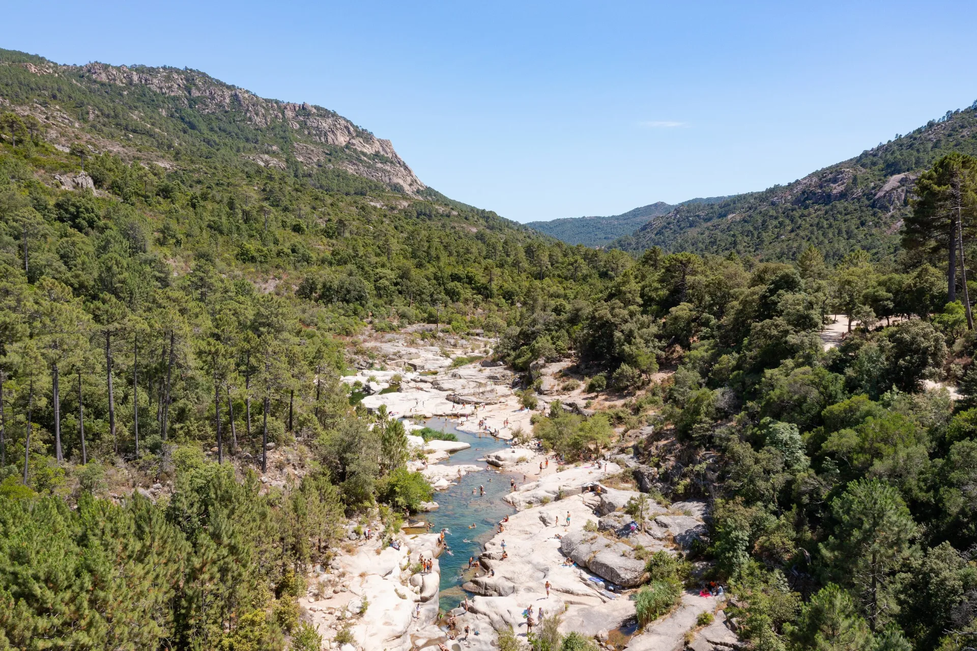 Vasques d'eau verte entre des dalles de granit clair dans la vallée boisée du Cavu, vues du ciel