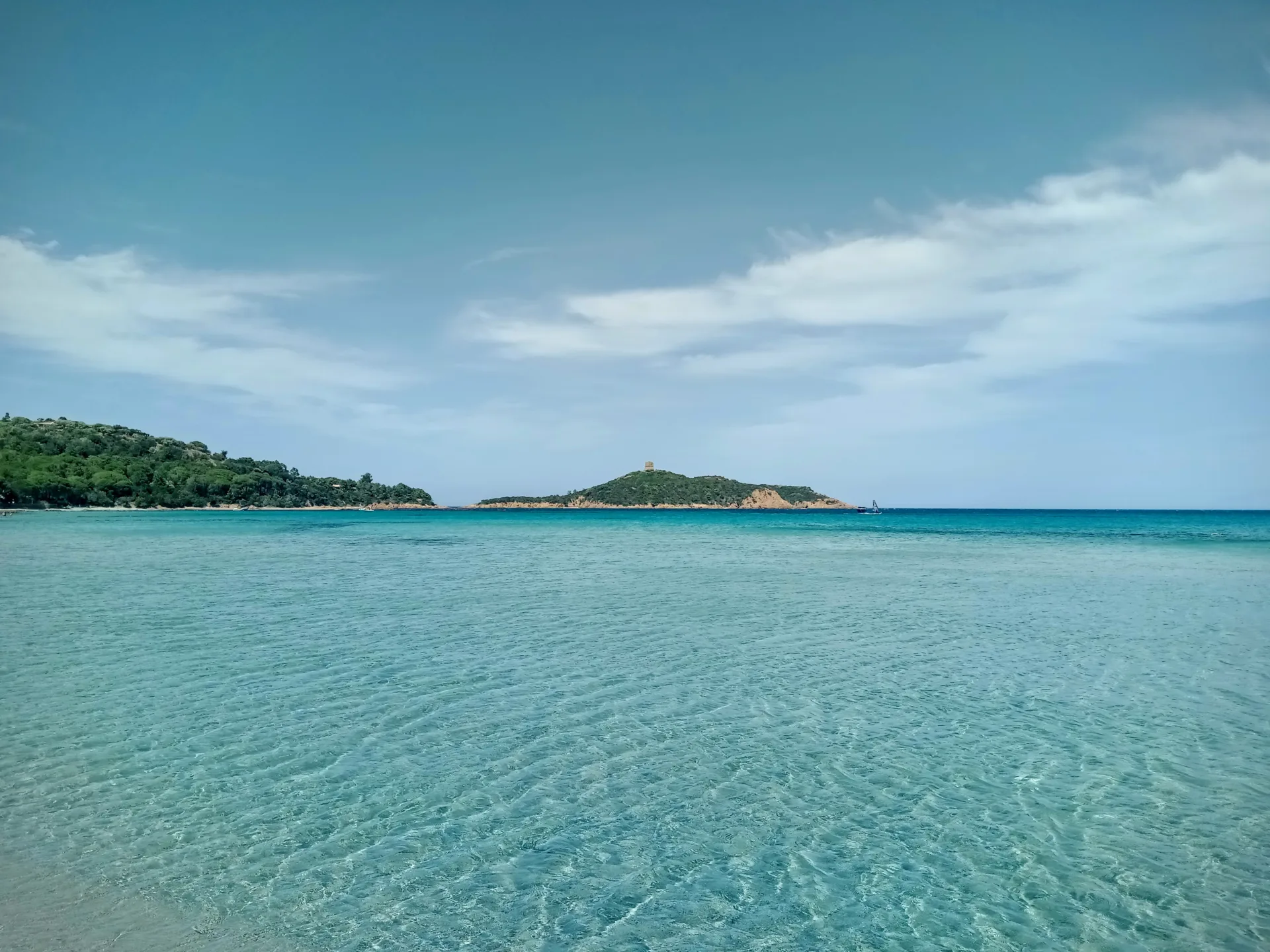 Eau turquoise peu profonde du golfe de Pinarellu et l'île de Pinarellu avec sa tour à l'horizon