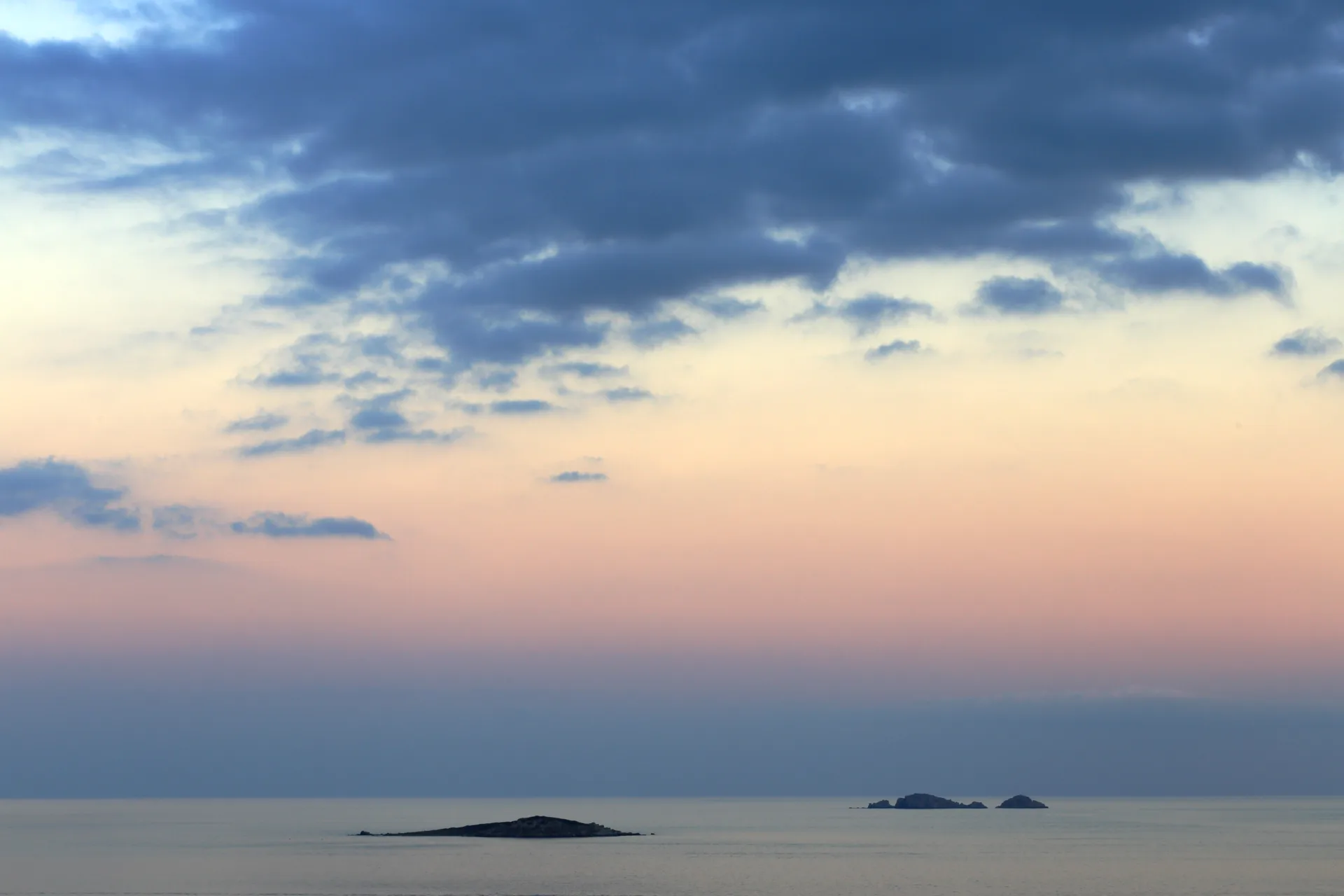 Les îles Cerbicale sur l'horizon au coucher du soleil, ciel rose et nuages sombres au-dessus de la mer