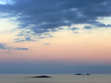 Les îles Cerbicale sur l'horizon au coucher du soleil, ciel rose et nuages sombres au-dessus de la mer