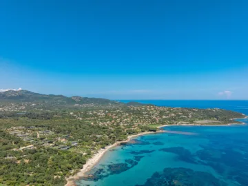 Vue aérienne d'une côte de maquis et de villas, avec une plage de sable et une eau turquoise, près de Pinarello