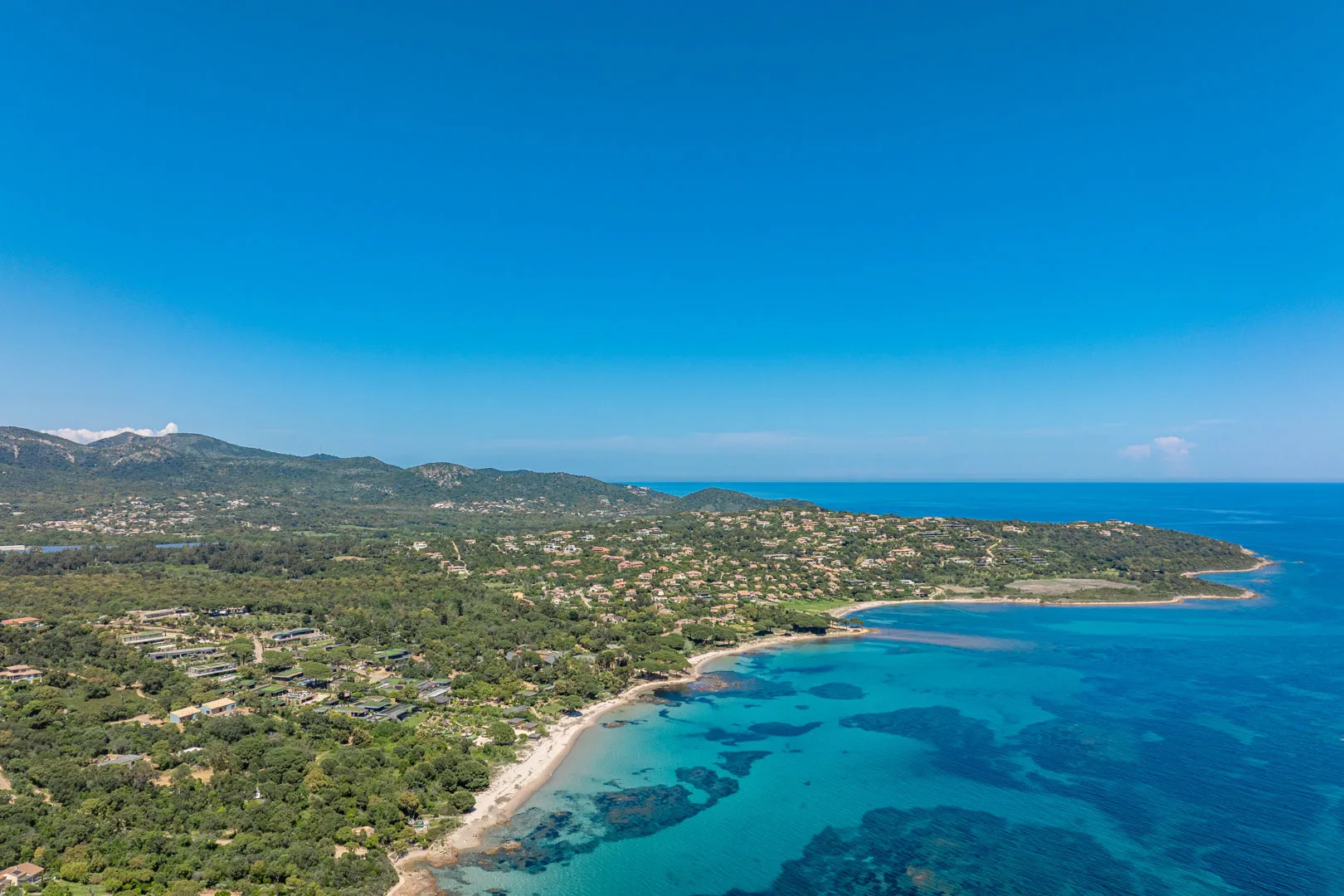 Vue aérienne d'une côte de maquis et de villas, avec une plage de sable et une eau turquoise, près de Pinarello