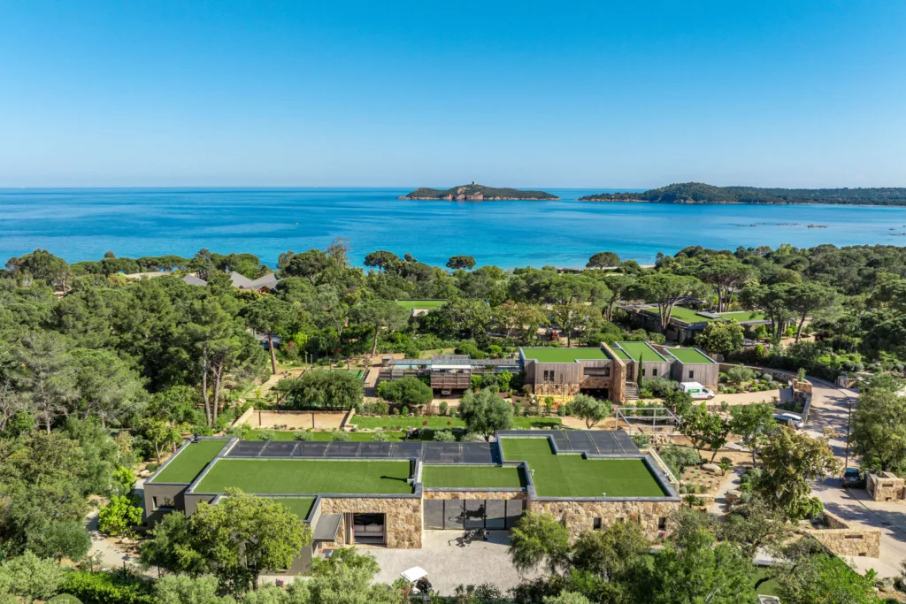 Vue aérienne de l'Hôtel Villa Padulaccia, toits végétalisés et murs de pierre dans les pins, golfe et île de Pinarellu au fond