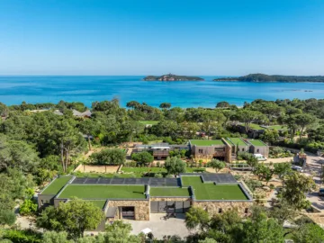 Vue aérienne de l'Hôtel Villa Padulaccia, toits végétalisés et murs de pierre dans les pins, golfe et île de Pinarellu au fond