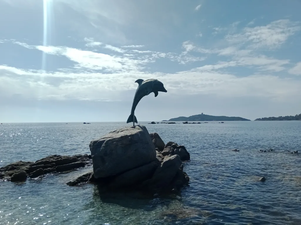 Sculpture en bronze d'un dauphin sur un rocher devant la plage du village de Pinarello, île de Pinarellu au loin